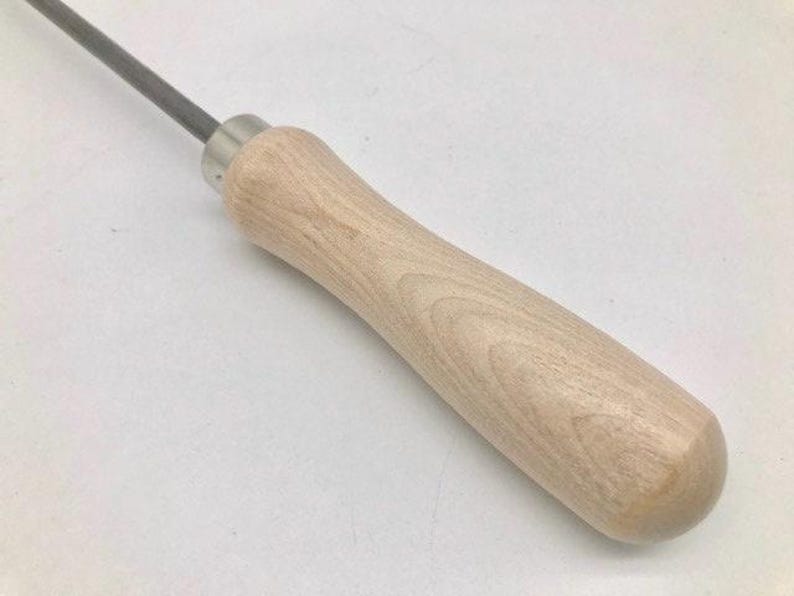 Op de afbeelding: Een close-up van een houten handvat bevestigd aan een metalen gereedschap. Het handvat is lichtbruin en heeft een gladde, afgeronde afwerking.