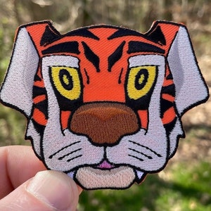 Op de afbeelding: Geborduurde patch met een tijgergezicht. De patch heeft de kleuren oranje, zwart, wit, bruin en geel. Het gezicht van de tijger is gedetailleerd met zwarte strepen, gele ogen en een bruine neus. Voor kleding of accessoires.