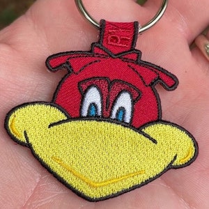 May include: A red and yellow cartoon bird keychain with a silver key ring. The bird has blue eyes and a yellow beak.
