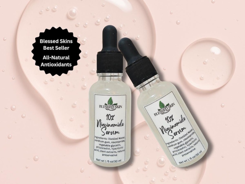 Op de afbeelding: Twee heldere glazen serumflessen met zwarte druppelaars op een lichtroze achtergrond. Elke fles heeft een wit etiket met de tekst "Blessed Skin 10% Niacinamide Serum". Een zwart rond etiket luidt "Blessed Skins Best Seller All-Natural Antioxidants".