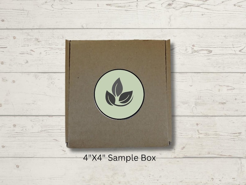 May include: A brown cardboard sample box, 4" x 4", with a circular logo featuring three stylized leaves in a light green circle. The box is centered on a light wood-grain surface.