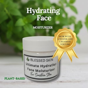 May include: A white jar of Blessed Skin Ultimate Hydration Face Moisturizer for Sensitive Skin. The jar has a white lid and a label with text. A gold seal reads "Now with a silkier and creamier texture." The words "Hydrating Face" and "Plant-Based" are also visible.