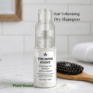 May include: A clear bottle of "Hair Volumizing Dry Shampoo" from "THE MANE EVENT" with a pump dispenser. The label reads "pure & organic" and "Plant-Based". A wooden hairbrush with dark bristles sits next to the bottle.