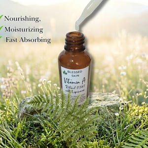 May include: An opened bottle of Vitamin A Retinol showing the dropper and product in a grassy field.  The product benefits are that it's nourishing, moisturizing, and absorbs quickly.