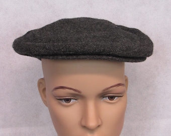 May include: A dark gray, flat cap made of a textured fabric. The cap has a rounded crown and a small, stiff brim. The hat is displayed on a mannequin head.