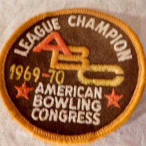 May include: A vintage, circular patch with a brown background and an orange border. The patch features the text "LEAGUE CHAMPION" and "AMERICAN BOWLING CONGRESS" in white. The letters "ABC" are in orange and yellow, with the year "1969-70" below. Two orange stars are also present.