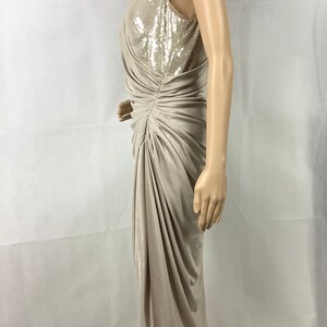 May include: A beige, sleeveless dress with a knee-length hemline. The bodice features a sequined panel, and the dress has a draped, ruched design. The dress is displayed on a mannequin against a white background.
