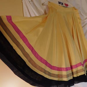 May include: A flowing yellow skirt with a wide, striped hem. The stripes include black, brown, pink, and tan. The skirt is made of a lightweight fabric and is hanging on a hanger.