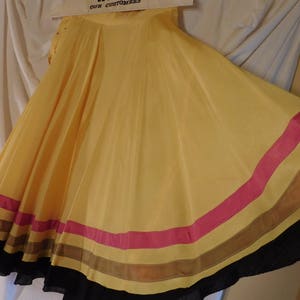 May include: A flowing, yellow skirt with a wide, flared design. The skirt features horizontal stripes of pink, brown, and black near the hem. The fabric appears lightweight and has a slight sheen.
