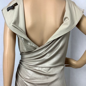 May include: A beige, draped evening gown with a cowl neckline and a low back. The dress features a sequined panel and a zipper closure. The label reads "Adrianna Papell". The dress is displayed on a mannequin.