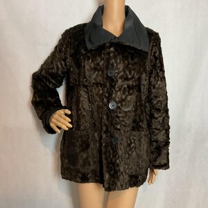 May include: A dark brown textured faux fur jacket featuring a solid black collar and three black buttons down the front. The jacket has long sleeves and a straight hemline, displaying a consistent deep brown color throughout the main body fabric.