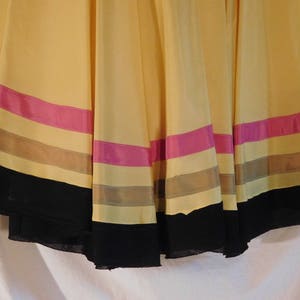 May include: A flowing, yellow skirt with horizontal stripes of pink, tan, and black. The skirt appears to be made of a lightweight fabric, with a slight sheen. The hemline is finished with a wide black band.