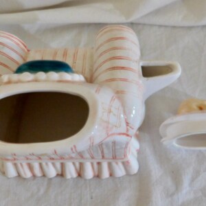 May include: A vintage ceramic teapot with a white base, adorned with red stripes and accents. The teapot features a teal-colored top and a matching lid. The design includes a scalloped edge and a handle.