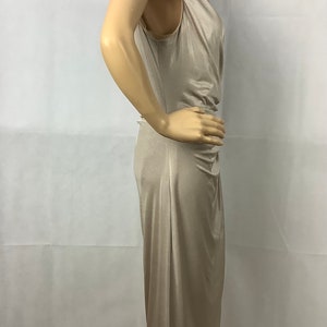 May include: A beige, sleeveless dress with a draped neckline and a knee-length hem. The dress has a fitted silhouette and a subtle sheen, suggesting a satin or silk-like fabric. The dress is displayed on a mannequin.