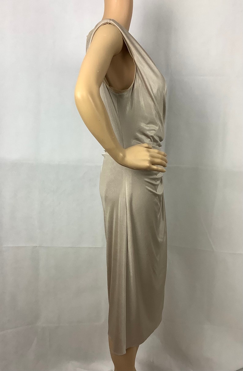 May include: A beige, sleeveless dress with a draped neckline and a knee-length hem. The dress has a fitted silhouette and a subtle sheen, suggesting a satin or silk-like fabric. The dress is displayed on a mannequin.