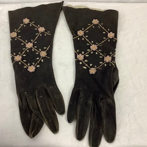 May include: A pair of black suede gloves with a floral design. The gloves feature a diamond pattern of pink flowers and gold beads on the upper portion. The gloves are long and elegant.