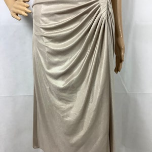 May include: A champagne-colored dress with a draped bodice and a knee-length skirt. The fabric has a subtle sheen, and the dress features a ruched detail on the side, adding texture and visual interest. The dress is displayed on a mannequin.