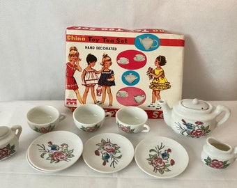 May include: A vintage China Toy Tea Set with hand-decorated floral designs. The set includes a teapot, creamer, cups, and saucers. The box features illustrations of children and tea sets. A charming collectible toy.