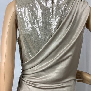 May include: A champagne-colored formal dress with a draped, asymmetrical design. The back of the dress features a sequined panel, and a zipper closure. The dress is sleeveless and appears to be made of a soft, flowing fabric.