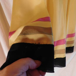 May include: Close-up of a yellow garment sleeve with horizontal stripes in pink, tan, and brown. The sleeve's cuff is black. The fabric appears to be silk or a similar lightweight material.