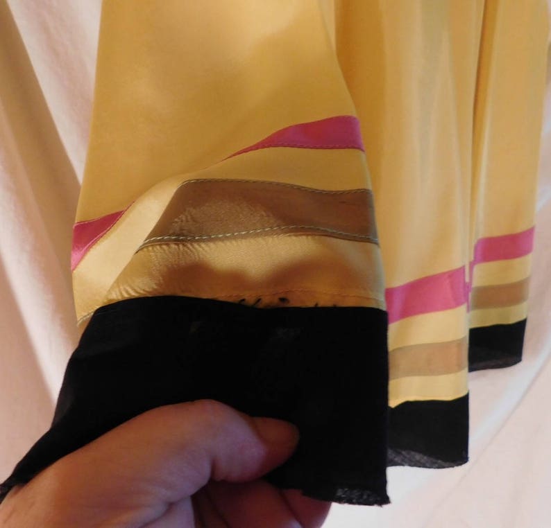 May include: Close-up of a yellow garment sleeve with horizontal stripes in pink, tan, and brown. The sleeve's cuff is black. The fabric appears to be silk or a similar lightweight material.