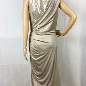 May include: A beige, sleeveless dress with a draped design. The back of the dress features a sequined panel. The dress has a knee-length hemline and is displayed on a mannequin.