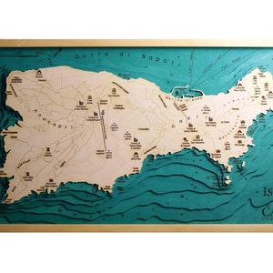 Könnte beinhalten: Eine dreidimensionale Holzkarte der Insel Capri, Italien. Die Karte ist in einem hellen Holzrahmen gerahmt und zeigt ein türkisfarbenes Meer mit braunen Linien, die die Tiefe darstellen. Die Insel ist in hellem Holz dargestellt, mit braunen Textbeschriftungen für verschiedene Orte.