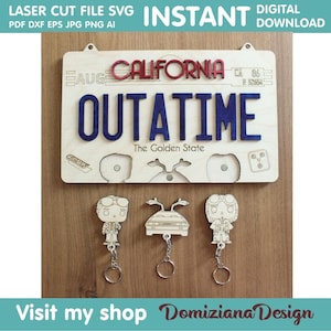 Può includere: Cartello in legno tagliato al laser con "OUTATIME" in lettere blu, "CALIFORNIA" in rosso e tre portachiavi. Il cartello include il testo "The Golden State" e "Download digitale istantaneo". I portachiavi presentano disegni di personaggi.