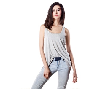 May include: A woman wearing a light gray tank top and light blue jeans. The tank top has a square neckline and a loose fit. The jeans are light wash with a straight leg. A dark blue belt is visible.