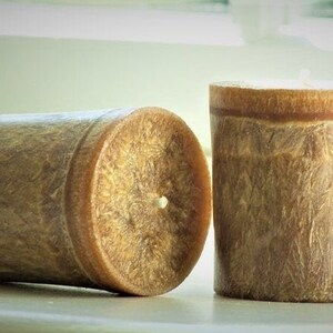 May include: Two brown votive candles with a textured surface. The candles are in a cylindrical shape and have a white wick.