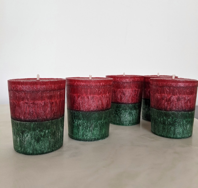 May include: Four red and green scented candles with a white wick in the center of each candle.