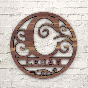 May include: A wooden round sign with a decorative letter C and the word "CEDAR" cut out. The sign has a wood grain pattern and is perfect for a home decor accent.