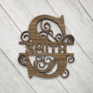 May include: A wooden cutout of the letter "S" with decorative swirls and the word "Smith" in the center. The cutout is brown and has a rustic appearance.