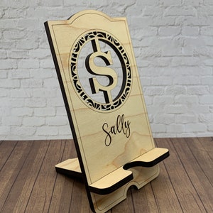 May include: Wooden phone stand with a cutout dollar sign design and the name "Sally" engraved on the front.