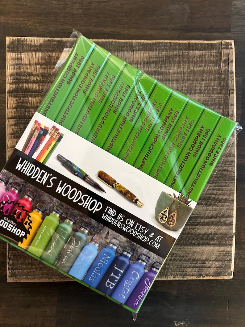 Pu&ograve; includere: Una collezione di borracce in acciaio inox personalizzate e colorate con diversi nomi. Le borracce sono disposte in fila su una superficie bianca con un cartello verde e dorato che recita "WHIDDEN'S WOODSHOP FIND US ON ETSY & AT WHIDDENSWOODSHOP.COM".