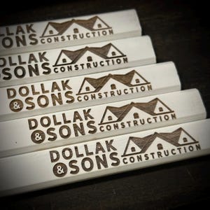 Pu&ograve; includere: Cinque matite di legno bianche con il testo "Dollak & Sons Construction" e un'icona di casa incisa su ogni matita.