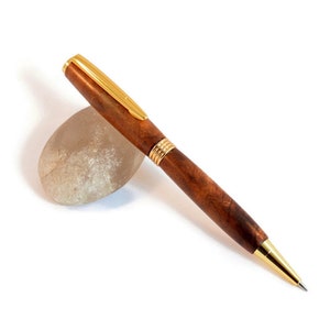 May include: A brown wooden pen with gold accents. The pen is lying on a white surface.