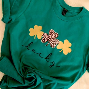 May include: A green t-shirt with a black and gold shamrock design and the word "lucky" written in black cursive.