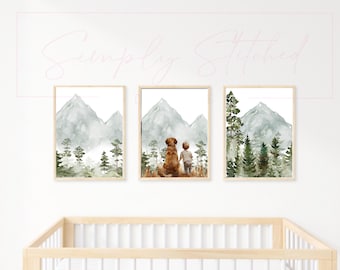 May include: Three watercolor prints featuring a mountain landscape with a dog and a child. The prints are framed in simple wooden frames and are hung on a white wall above a wooden crib.