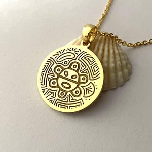 May include: A gold-colored pendant necklace featuring a circular pendant with an engraved design. The pendant hangs from a delicate gold chain. The design on the pendant is an intricate pattern with a central figure.