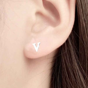 Peut inclure: Gros plan sur une oreille avec une petite boucle d'oreille en argent en forme de lettre V.