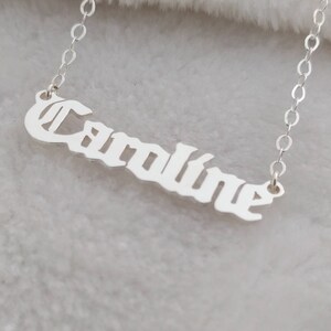 Puede incluir: Collar de plata con el nombre "Caroline" escrito en fuente gótica.