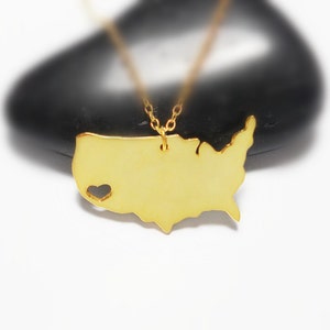 May include: Gold necklace featuring a pendant shaped like the outline of the United States with a heart cut out in the center.