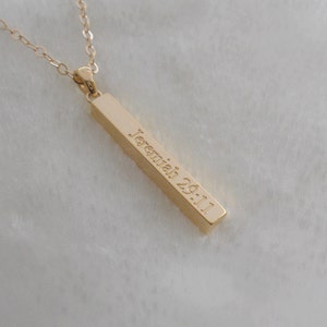 Puede incluir: Collar de oro con un colgante de barra grabado con el texto "Jerem&iacute;as 29:11".