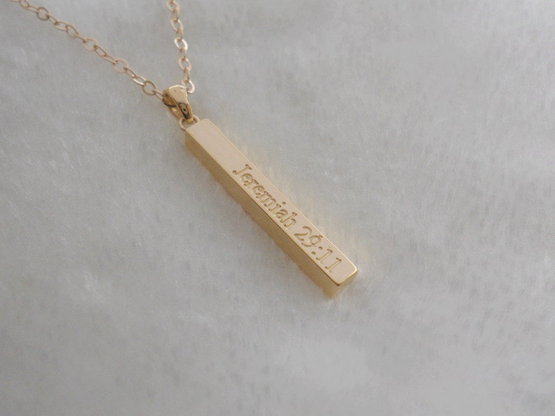 Puede incluir: Collar de oro con un colgante de barra grabado con el texto "Jerem&iacute;as 29:11".