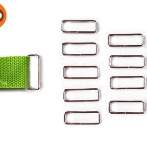 Könnte beinhalten: Zehn silberne Metall-Schiebeschließen für Riemen oder Gürtel. Die Schließen sind rechteckig mit abgerundeten Ecken und in zwei Reihen zu fünf angeordnet.