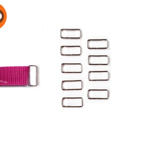 Könnte beinhalten: Ein Satz mit 10 silbernen Metall-Schiebeschließen für Riemen oder Gürtel. Die Schließen sind rechteckig und haben eine glatte Oberfläche. Die Schließen sind in zwei Reihen zu fünf angeordnet.