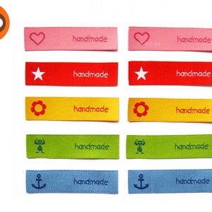 Peut inclure: Dix étiquettes en tissu colorées avec différents motifs brodés, dont un cœur, une étoile, une fleur, un extraterrestre et une ancre. Chaque étiquette porte l'inscription "handmade".