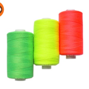 Pode incluir: Três carretéis de fio em cores verde brilhante, amarelo e laranja. Os carretéis são etiquetados com o site "NI-KO.de".