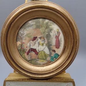 May include: A framed miniature painting depicting a scene with four figures in a wooded setting. The figures are dressed in 18th-century clothing and are engaged in a conversation. The painting is set in a gold frame with a raised lip.